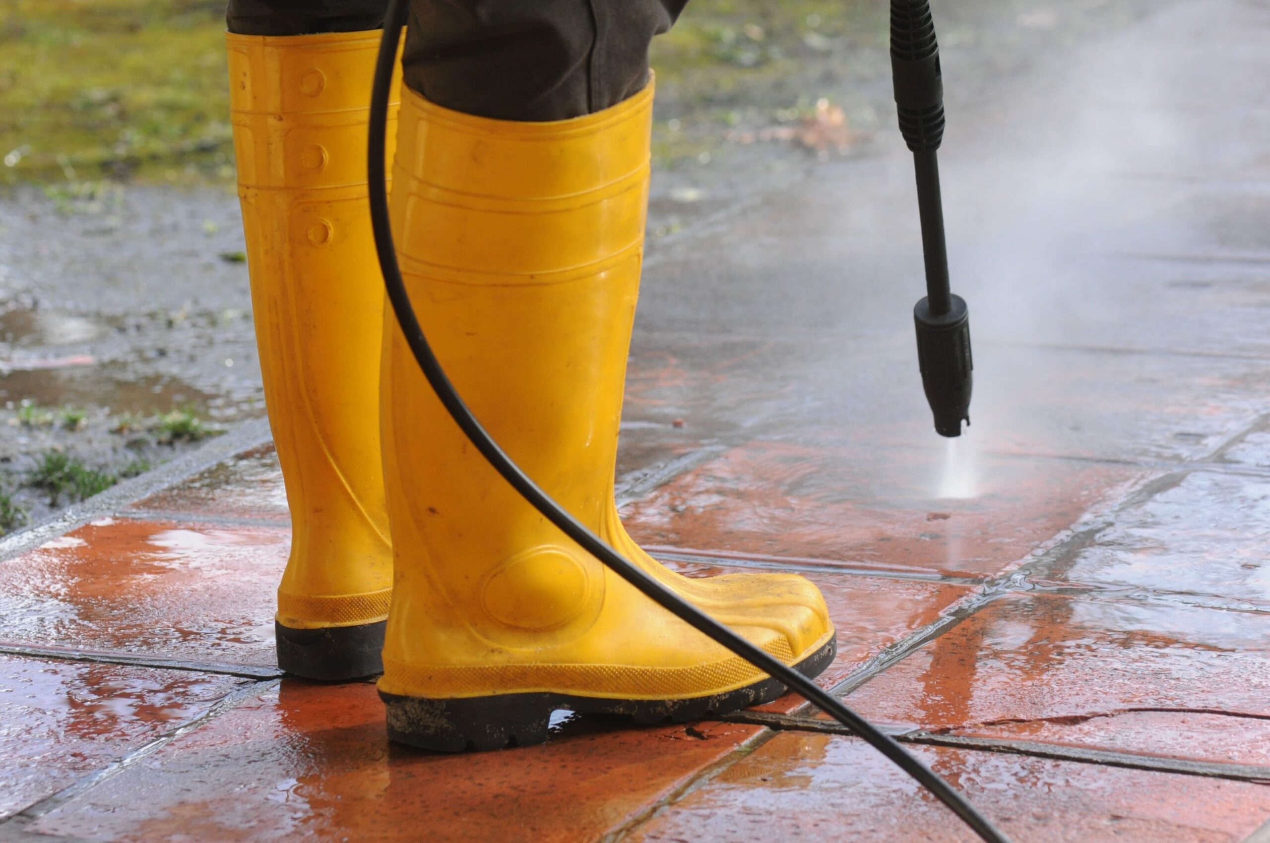 person-wearing-yellow-rubber-boots-with-high-pressure-water-nozzle-cleaning-dirt-tiles 1 Pressure Washing (concrete)